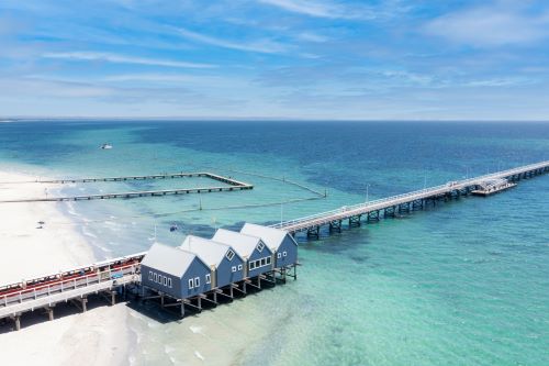A view of blue buildings on stilts over the ocean with a jetty