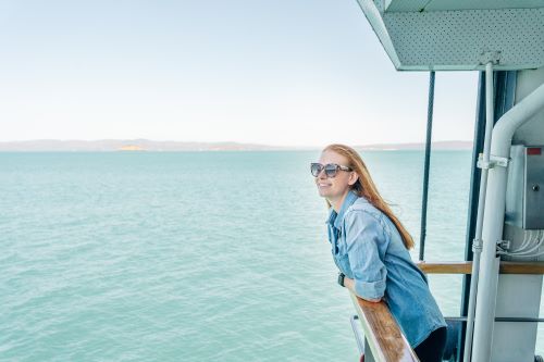 A traveller standing against the railings of a boat looking out to the ocean