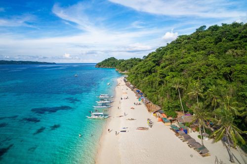 Aerial view of a tropical beach with turquoise water, white sand, boats near the shore, and lush green hills