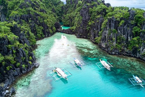 Aerial view of turquoise waters and limestone cliffs in El Nido, Palawan, with boats on the lagoon