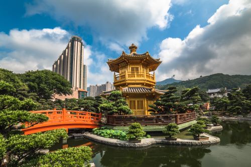 A golden pavilion surrounded by lush green gardens and high city buildings in the background