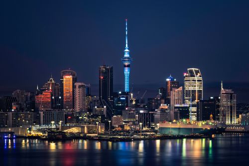 Auckland skyline at night featuring the illuminated Sky Tower with city lights reflecting on the harbour.