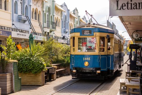 A vintage blue tram moves through a lively street lined with colourful buildings.