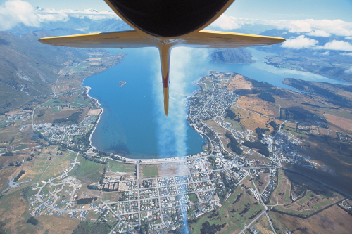 A shot from a plane mounted camera of the Wanaka airshow grounds and the tail of the plane leaving a smoke trail