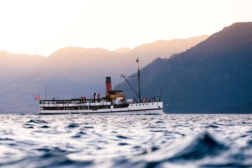 Vintage steamship cruising across a lake with mountains in the background at sunset.