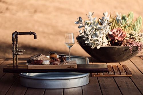 A rustic bathtub set up with a spread and glass of wine and some succulent plants in the backgorund. 