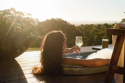 A woman from the back sitting in a rustic bathtub enjoying a glass of wine and the view. 