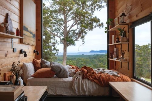 Heyscape cabin from inside with a cozy bed in front of a large window overlooking beautiful nature. 