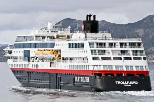 Large Hurtigruten cruise ship sailing near mountainous coastline