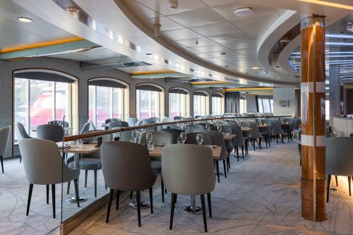 Elegant cruise ship dining room with tables and chairs.