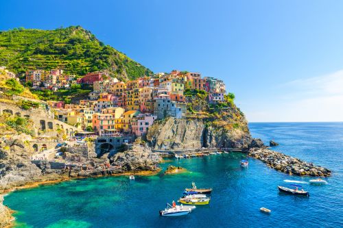 Typical Italian village in Cinque Terre with multi-coloured houses built on cliffs and fishing boats in the bay