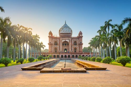 An elegant sandstone and marble mausoleum with an imposing dome, intricate arches, and symmetrical gardens towards a blue sky