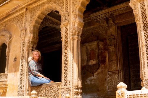 A woman sitting in the arched window of an ornate, carved sandstone building.