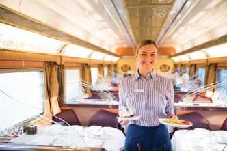 A waitress in the onboard Queen Adelaide Restaurant holding two plates and smiling into the camera