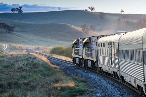 Indian Pacific curving through misty countryside with soft light and distant hills.