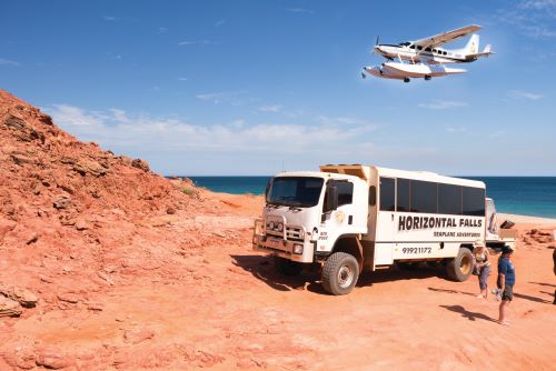 The Horizontal Falls touring bus parked on the red cliffs with the ocean in the background the seaplane flying above the bus