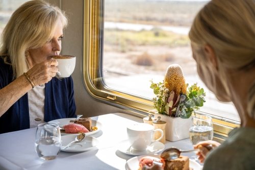 Train passengers enjoying afternoon tea and looking outside the window. 