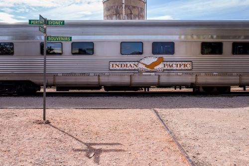 Silver Indian Pacific train beside a signpost pointing to Perth, Sydney, and Souvenirs.