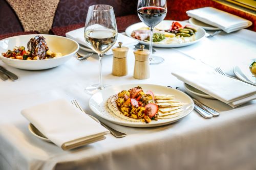 Close up of a dining table set up with plates with food and filled wine glasses