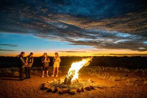 Tourists standing around a fire in the outback at sunrise. 