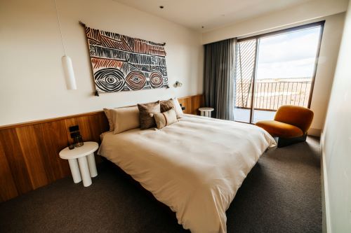 Modern, stylish hotel room with neutral tones, Indigenous-inspired wall art, and a large bed.