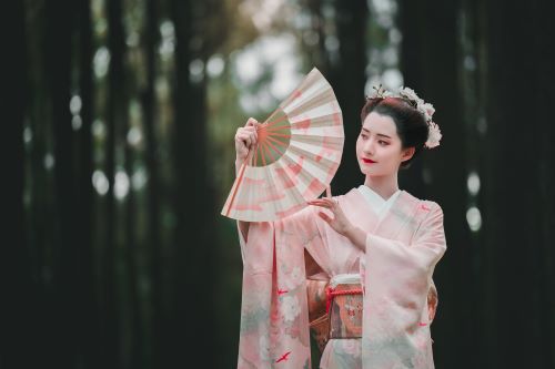 Elegant Woman in Kimono Holding Fan Amidst Serene Forest Background.