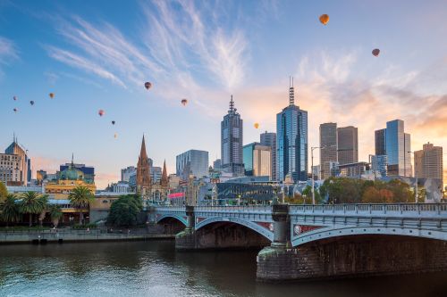 Melbourne skyline at sunset with river, bridge, and hot air balloons