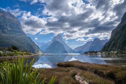 Mountain valley reflected in calm water under a cloudy sky.