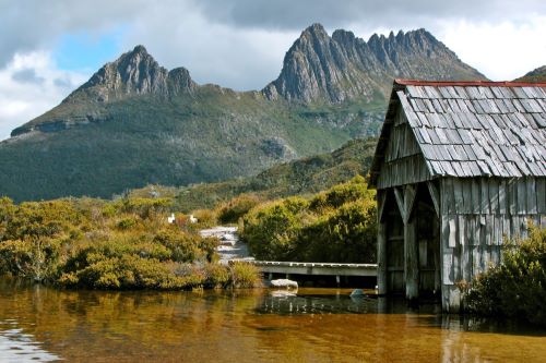 A boathouse by the lake with Cradle Mountain toweing in the background.