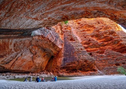 The red walls of Cathedral Gorge in the Kimberley with people sitting around the waterhole enjoying the views 