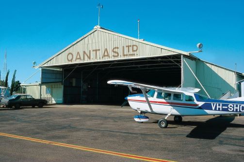 An open, empty hangar labelled as Qantas LTD and a Cessna in front of it