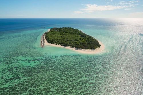 Small tropical island surrounded by clear blue water and visible coral reefs.