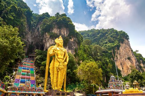 Large golden statue in front of steep, colorful temple steps and limestone cliffs