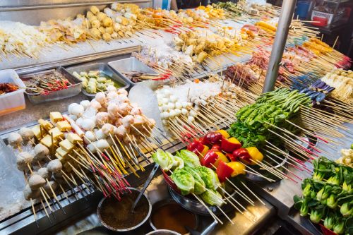 Assorted skewered foods displayed on ice at a busy street market stall