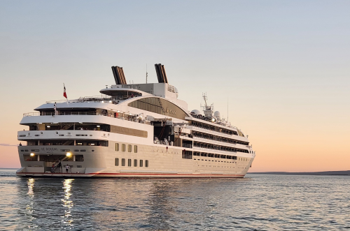 Le Soleal sailing at sunset with warm orange-pink sky and calm waters.