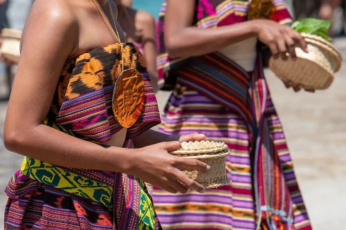 People wearing colorful traditional woven clothing holding small woven baskets
