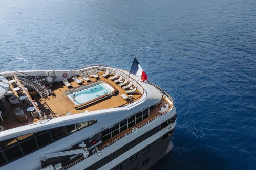 Cruise ship deck with a swimming pool and sun loungers overlooking calm blue ocean waters
