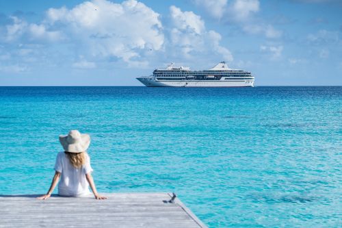 Person sitting on a wooden deck overlooking turquoise ocean with a cruise ship in the distance.