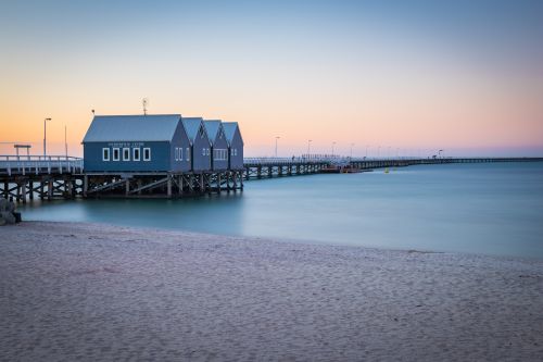 Wooden jetty with blue boathouses extending over calm water at sunset