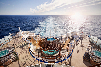 An architectural shot of the pool deck with three whirlpools overlooking the vast ocean from the back of the cruise ship