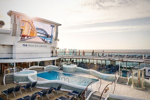 The pool deck with lots of sun lounges, a big screen and two hot tubs next to the pool