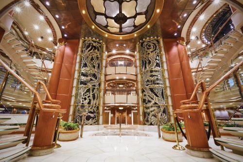 Atrium of a cruise ship with stairs on either side and lifts with brown interior