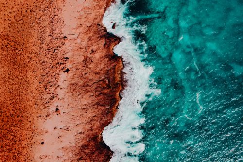 Aerial view of rugged red coastline meeting turquoise ocean waves