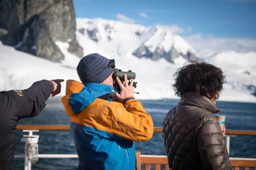 Passengers standing onboard one of Quark Expedition's vessel looking out to the sea and land covered by ice