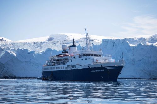 Quark Expedition's vessel Ocean Adventurer at sea in front of huge icebergs that seem higher than the vessel itself