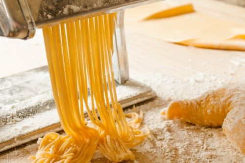 A close-up sot of spaghetti coming out from a pasta maker onto a table covered with flower and dough