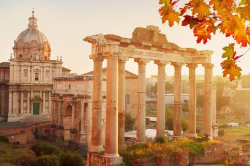 Historical buildings and ancient Roman columns in the Roman Forum coloured in golden autumn lights and a branch with orange leaves cutting into the photo from the right top corner