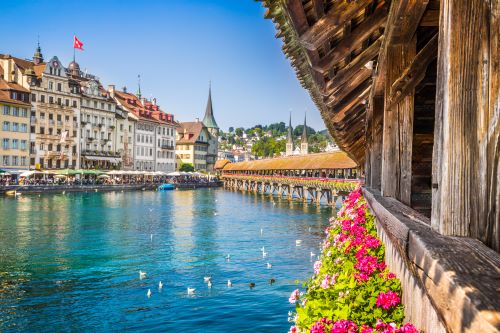 The Kapellbrücke, a covered wooden footbridge spanning the river diagonally in the city of Lucerne with the iconic buildings in the background