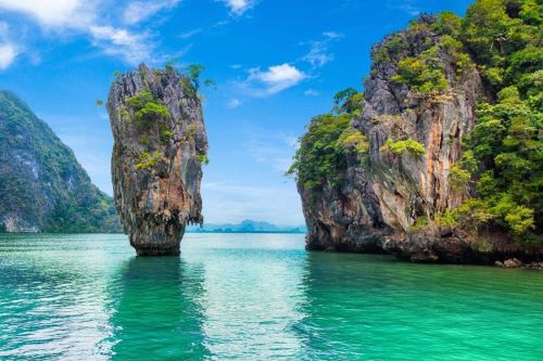 The iconic James Bond Island in Phuket with its towering limestone karst rising dramatically from the emerald-green waters, surrounded by lush, rocky cliffs.