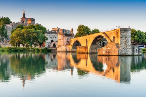 An old historic bridge in Europe reflecting onto the water with an old castle in the background 